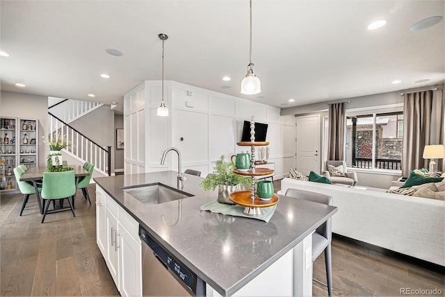 kitchen featuring a sink, open floor plan, hanging light fixtures, stainless steel dishwasher, and an island with sink