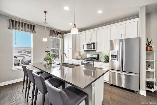 kitchen with stainless steel appliances, a sink, white cabinets, hanging light fixtures, and an island with sink