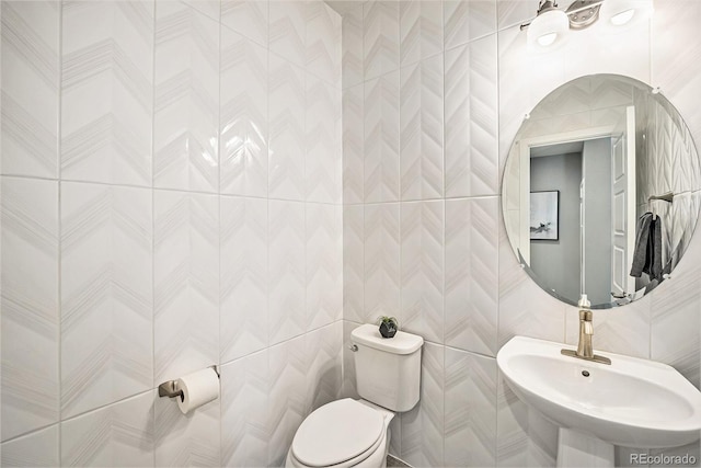 bathroom with a sink, toilet, and tile walls