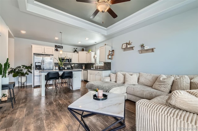 living room with dark wood-style floors, a tray ceiling, ceiling fan, and recessed lighting