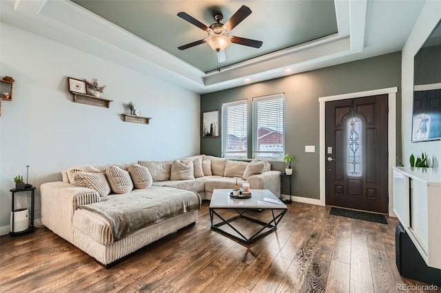 living area with a tray ceiling, dark wood-style flooring, a ceiling fan, and baseboards