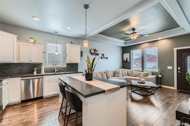 kitchen featuring dark wood-style flooring, a sink, stainless steel dishwasher, tasteful backsplash, and dark countertops