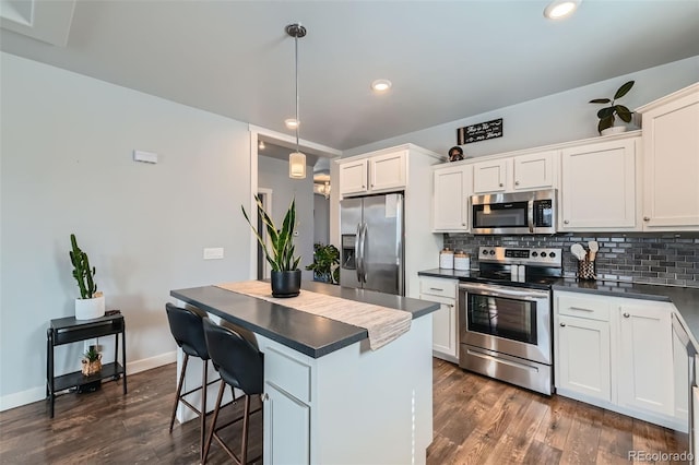 kitchen featuring dark wood-type flooring, a kitchen island, appliances with stainless steel finishes, backsplash, and dark countertops