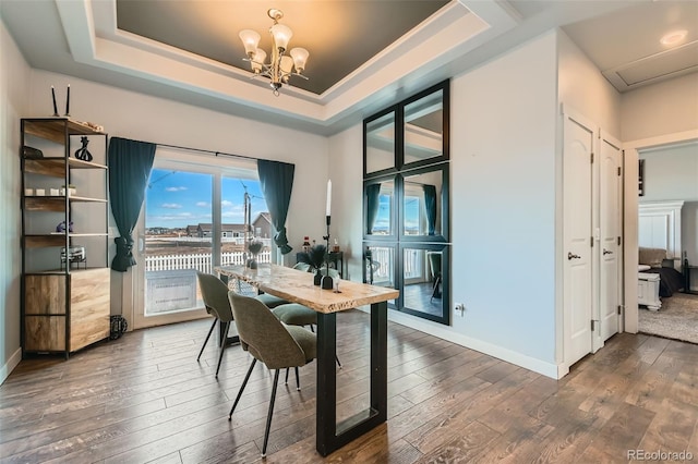 dining area featuring a notable chandelier, baseboards, a raised ceiling, and hardwood / wood-style floors