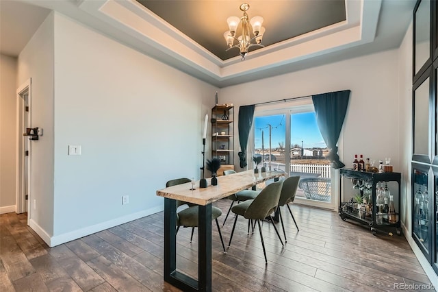 dining area featuring dark wood-type flooring, a raised ceiling, a notable chandelier, and baseboards