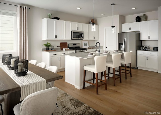 kitchen featuring a breakfast bar, a kitchen island with sink, appliances with stainless steel finishes, white cabinets, and light wood finished floors