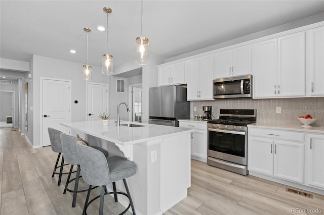 kitchen with sink, hanging light fixtures, a center island with sink, stainless steel appliances, and white cabinets