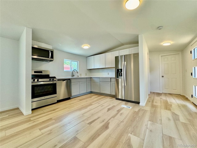 kitchen featuring lofted ceiling, sink, appliances with stainless steel finishes, and light hardwood / wood-style floors