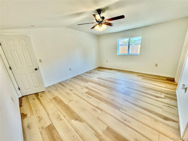 empty room with a textured ceiling, ceiling fan, vaulted ceiling, and light hardwood / wood-style floors