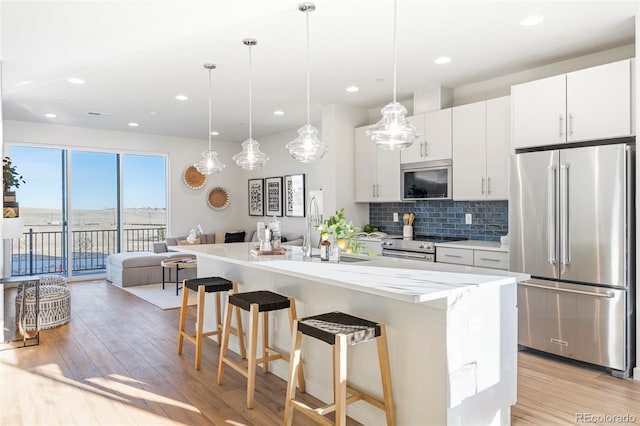 kitchen with a kitchen island with sink, stainless steel appliances, white cabinets, open floor plan, and hanging light fixtures