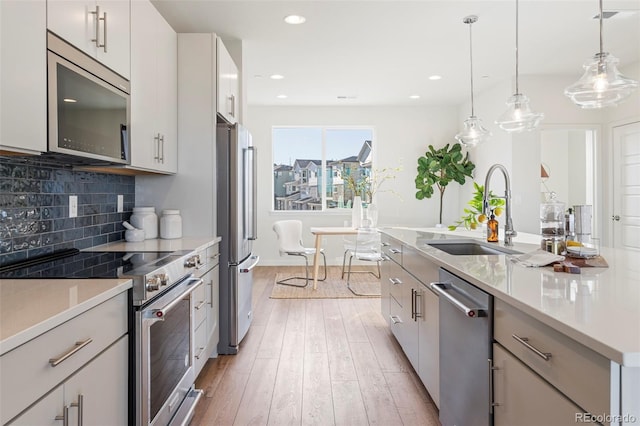 kitchen featuring appliances with stainless steel finishes, light countertops, white cabinetry, pendant lighting, and a sink