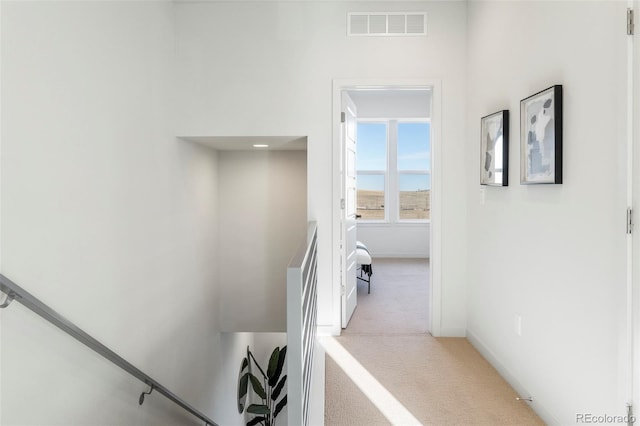 hall with baseboards, visible vents, and light colored carpet