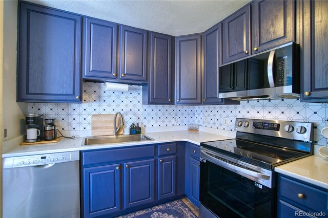 kitchen featuring light countertops, blue cabinetry, tasteful backsplash, appliances with stainless steel finishes, and a sink