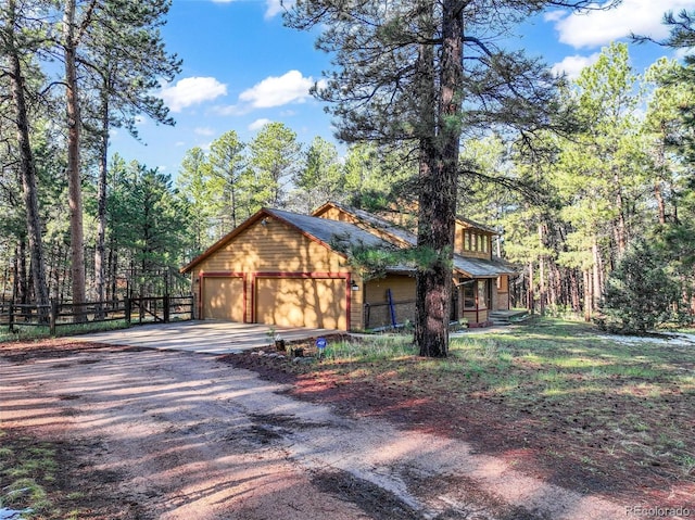 view of home's exterior with driveway, fence, a garage, and a view of trees