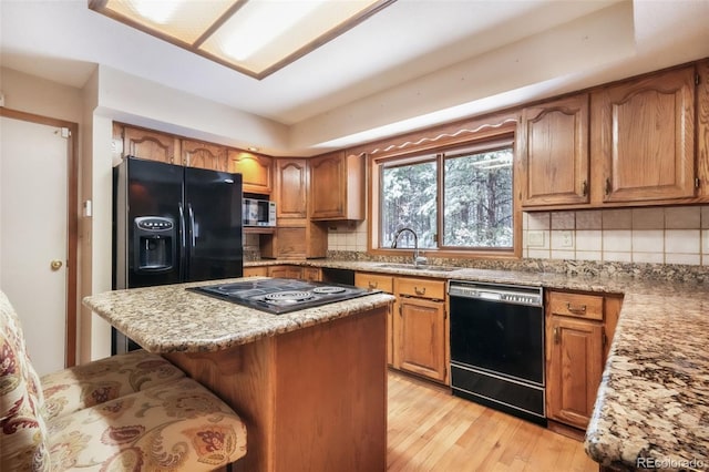 kitchen with black appliances, a sink, decorative backsplash, a breakfast bar, and light wood-type flooring