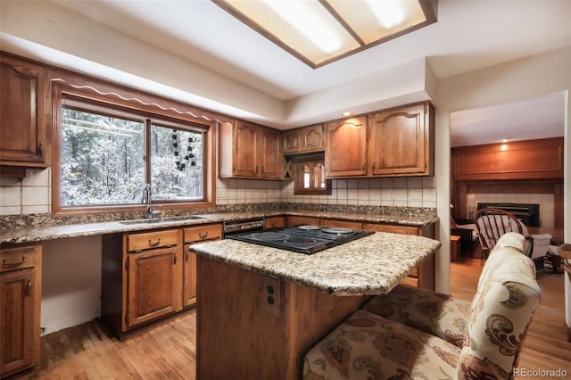 kitchen featuring a sink, black electric cooktop, light wood-style flooring, brown cabinets, and tasteful backsplash