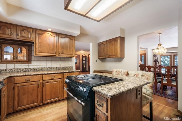 kitchen with black range with electric stovetop, a chandelier, brown cabinetry, and light wood-style floors