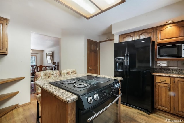 kitchen with black appliances, a center island, brown cabinets, light wood-type flooring, and light stone countertops