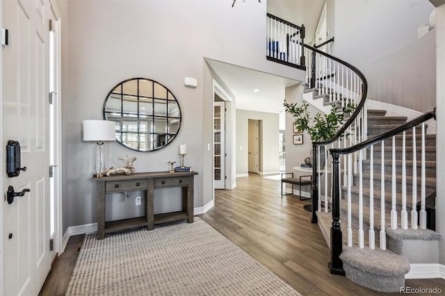 entryway with a high ceiling, stairway, wood finished floors, and baseboards