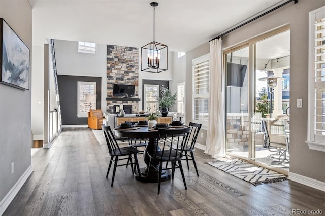 dining room with a notable chandelier, a stone fireplace, baseboards, and wood finished floors