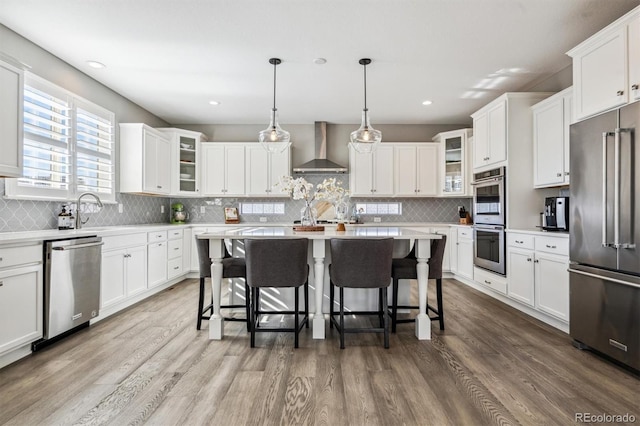 kitchen featuring wall chimney range hood, stainless steel appliances, light countertops, and decorative light fixtures