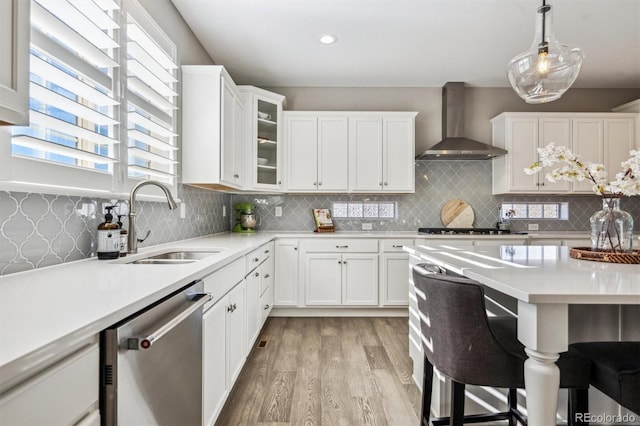 kitchen featuring stainless steel appliances, wall chimney range hood, light countertops, and glass insert cabinets