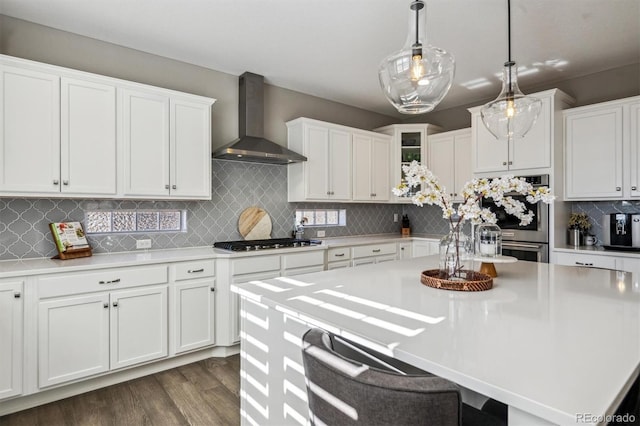 kitchen featuring pendant lighting, light countertops, wall chimney exhaust hood, and white cabinetry