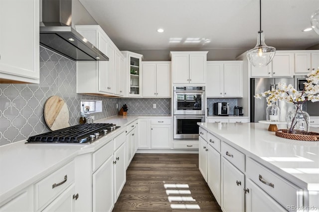 kitchen featuring wall chimney exhaust hood, glass insert cabinets, decorative light fixtures, light countertops, and stainless steel appliances