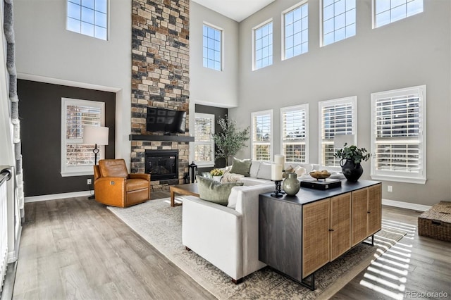 living area featuring a stone fireplace, light wood-type flooring, and baseboards