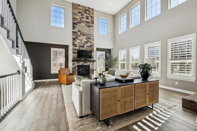 living area with a stone fireplace, a healthy amount of sunlight, wood finished floors, and baseboards