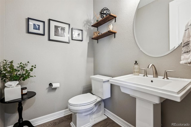 half bath with toilet, baseboards, and wood finished floors