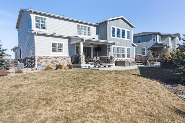 back of house with stone siding, a yard, board and batten siding, and a patio