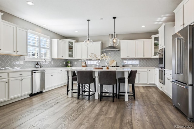 21854 Tyrolite Ave, Parker, CO 80138 - kitchen with appliances with stainless steel finishes, wall chimney range hood, a kitchen bar, decorative backsplash, and white cabinetry