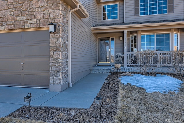 doorway to property featuring a garage, stone siding, a porch, and roof with shingles