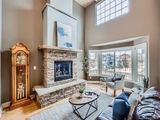 living area featuring a fireplace, a towering ceiling, baseboards, and wood finished floors