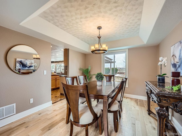 dining area with a tray ceiling, light wood finished floors, visible vents, an inviting chandelier, and baseboards