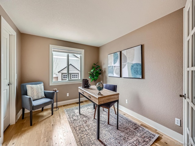 home office featuring light wood-style flooring, baseboards, and a textured wall