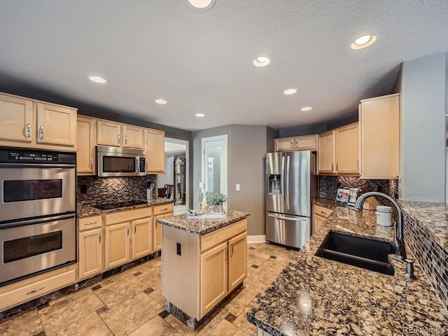 kitchen with appliances with stainless steel finishes, dark stone counters, light brown cabinets, and a sink