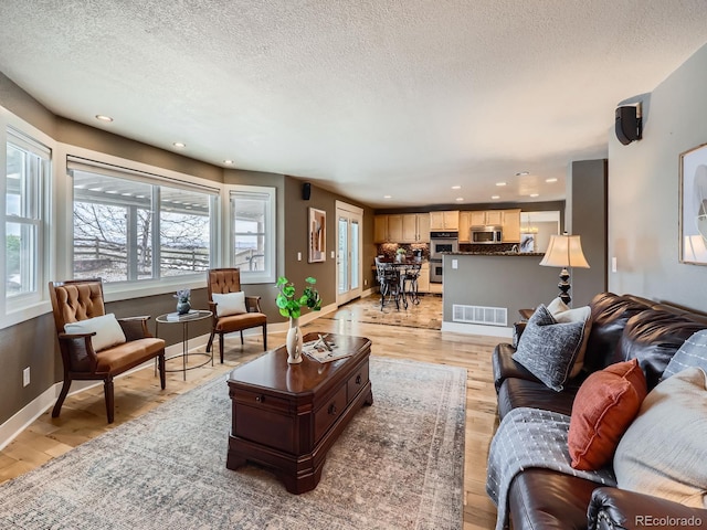 living room featuring light wood finished floors, baseboards, visible vents, a textured ceiling, and recessed lighting