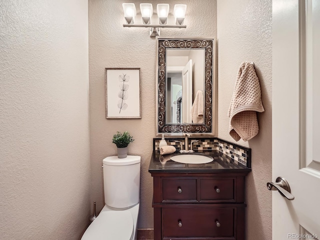 bathroom with toilet, a textured wall, backsplash, and vanity