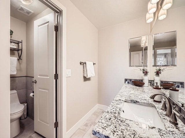 bathroom with double vanity, baseboards, visible vents, toilet, and a sink