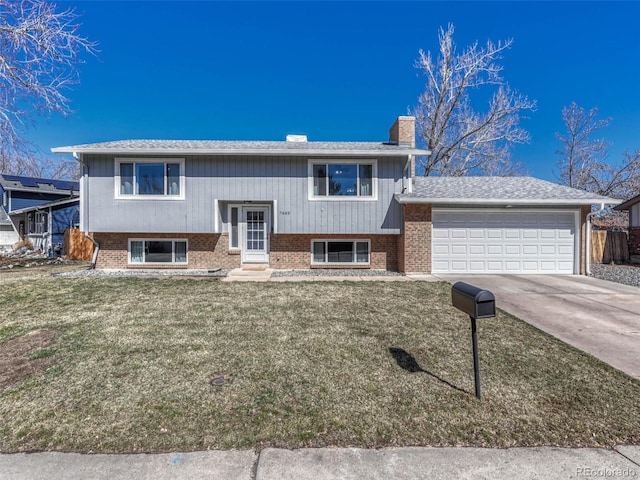 bi-level home featuring a garage, concrete driveway, a chimney, a front lawn, and brick siding