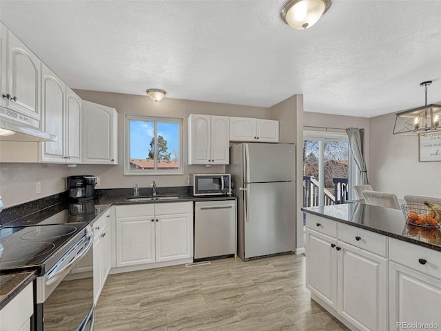 kitchen featuring white cabinets, dark stone countertops, stainless steel appliances, under cabinet range hood, and a sink