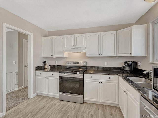 kitchen featuring white cabinets, dark stone countertops, stainless steel appliances, under cabinet range hood, and a sink