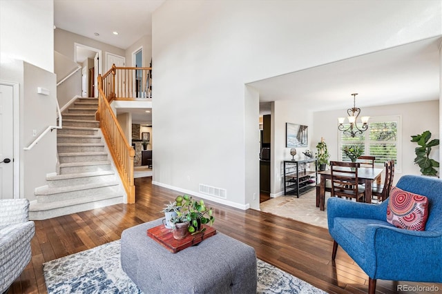 living room with hardwood / wood-style flooring, stairs, a chandelier, a high ceiling, and baseboards
