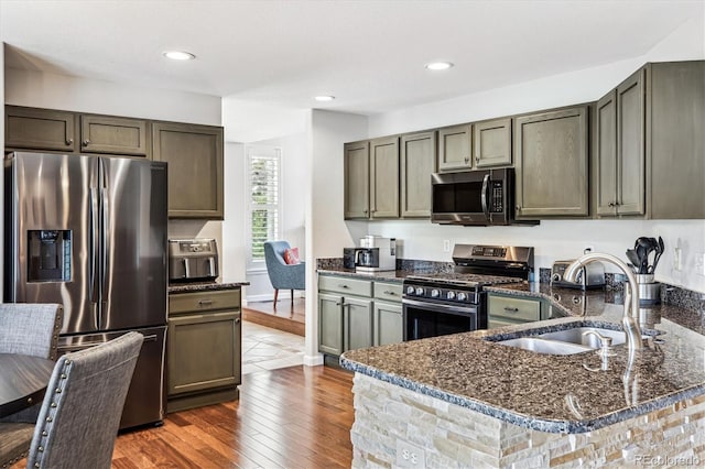 kitchen with stainless steel appliances, a sink, dark stone counters, a peninsula, and dark wood-style flooring