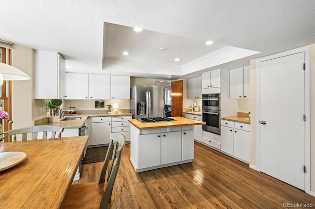 kitchen with a center island, a raised ceiling, appliances with stainless steel finishes, a sink, and butcher block countertops