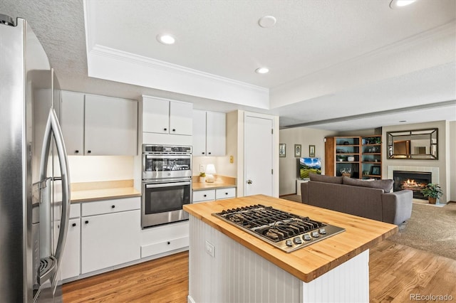 kitchen with stainless steel appliances, a tray ceiling, wood counters, and crown molding