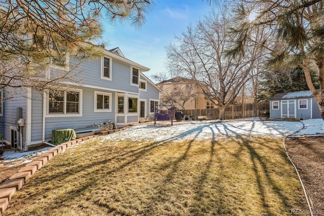 snow covered house with a storage shed, a lawn, an outbuilding, and fence