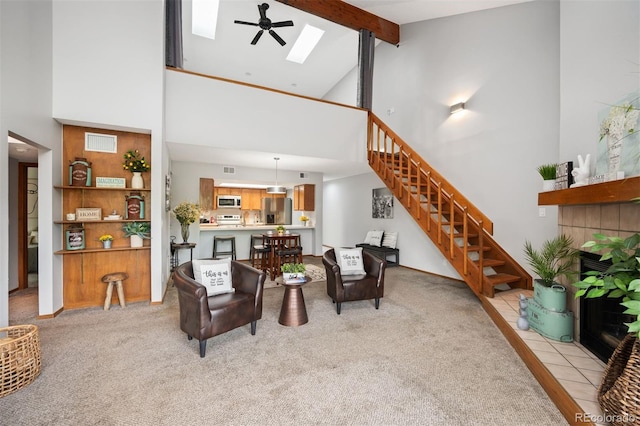 living room with a skylight, beamed ceiling, high vaulted ceiling, a tiled fireplace, and ceiling fan